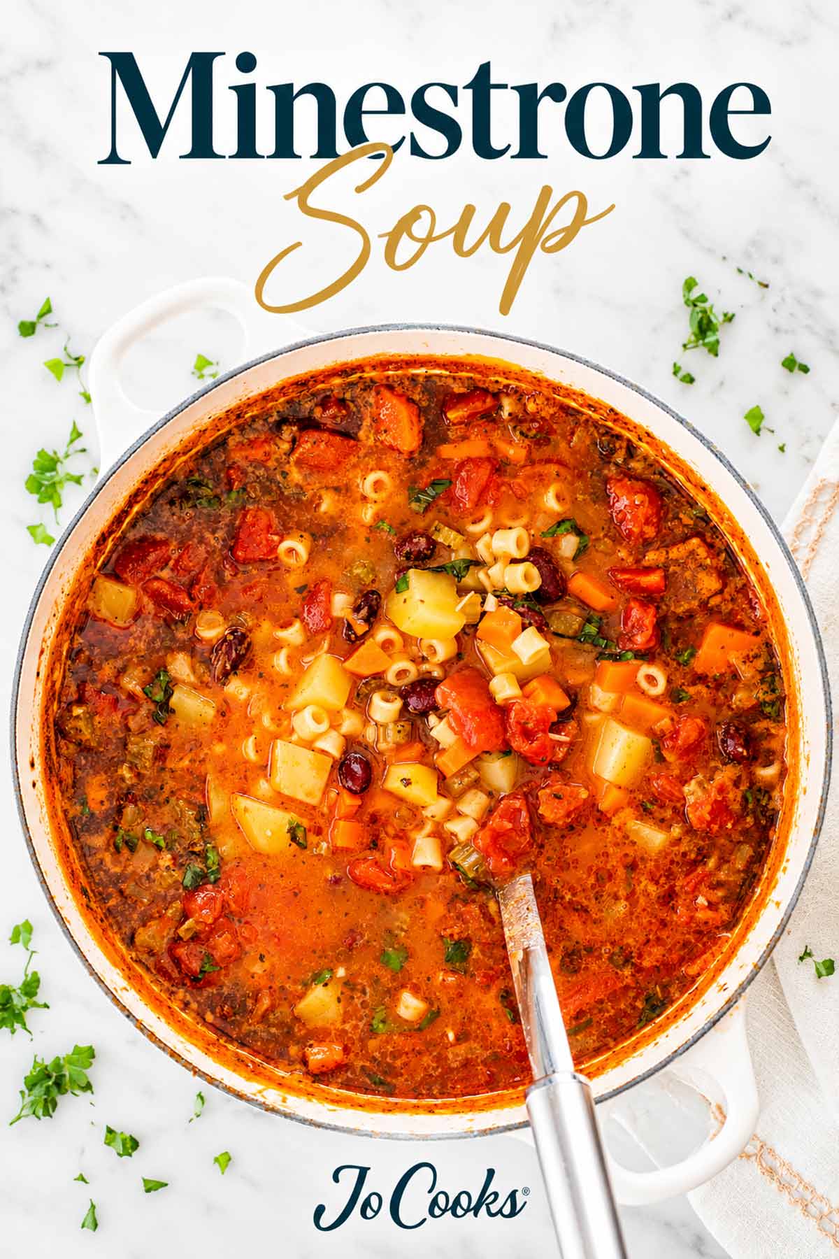 Overhead view of minestrone soup in a white Dutch oven with a ladle, recipe title and Jo Cooks logo.