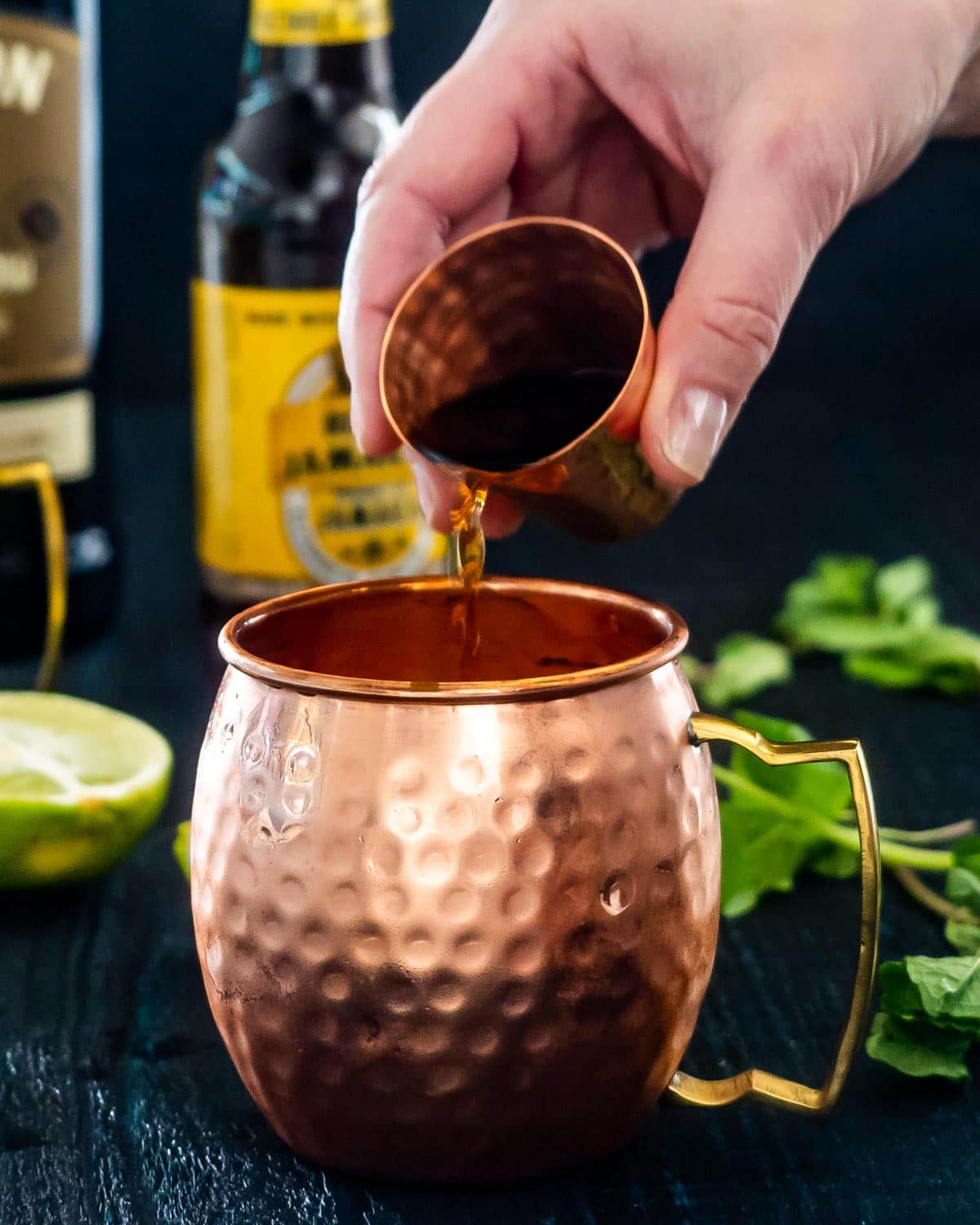 a hand pouring irish whiskey in a copper cup.