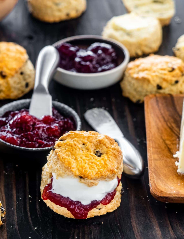 an irish scone cut in half with butter, raspberry jam and whipped cream.