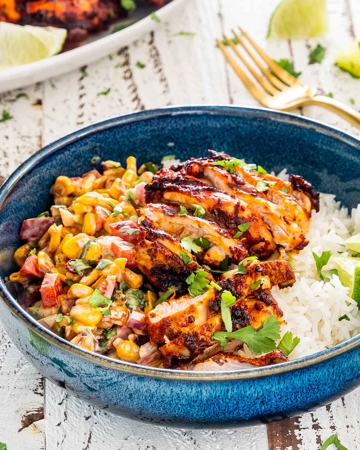 pollo asado in a blue bowl on a bed of rice with a serving of mexican street corn salad.