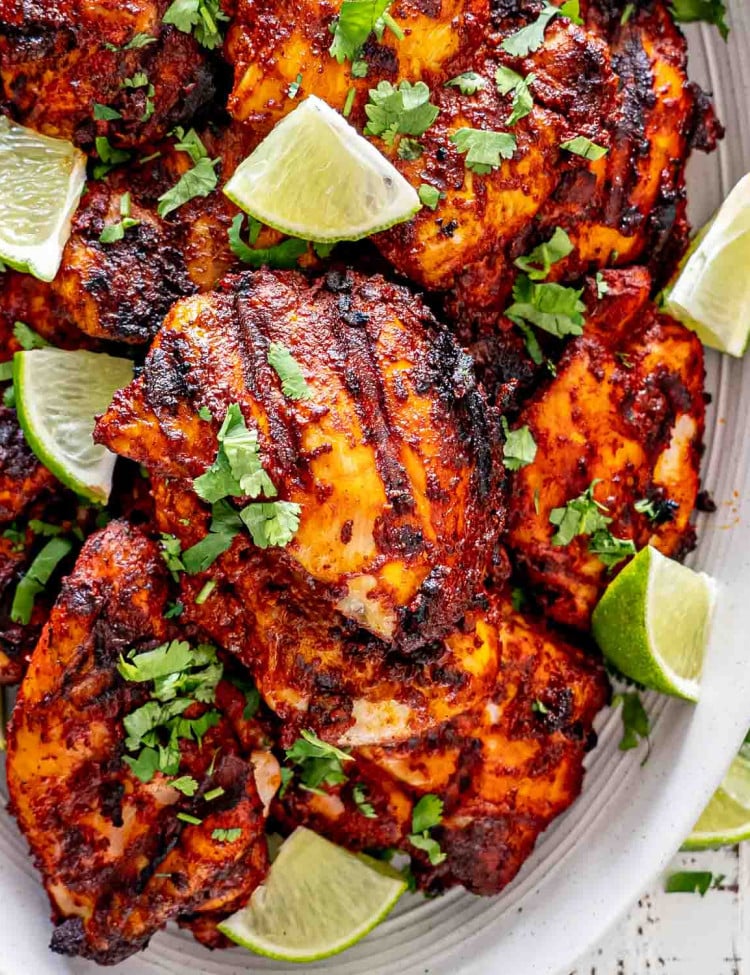 grilled pollo asado on a white platter garnished with cilantro and lime wedges.