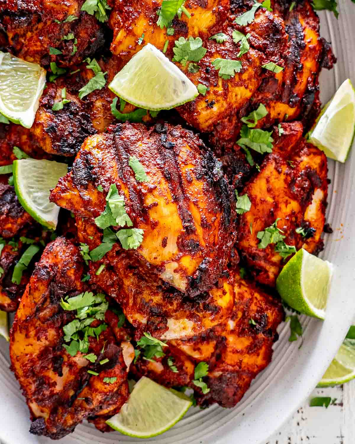 grilled pollo asado on a white platter garnished with cilantro and lime wedges.