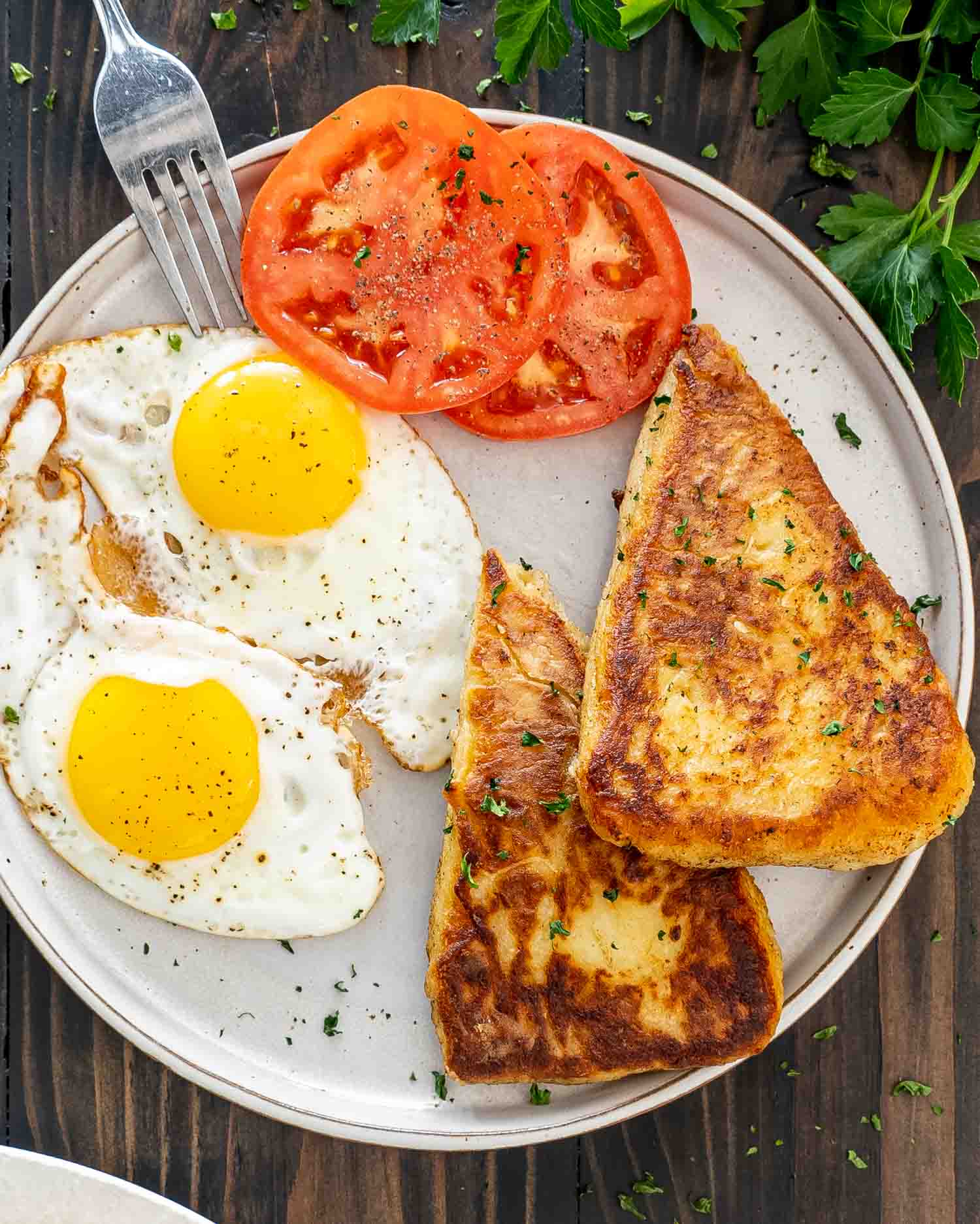 two irish potato cakes (potato farls) on a plate with sunny side up eggs and two tomato slices.