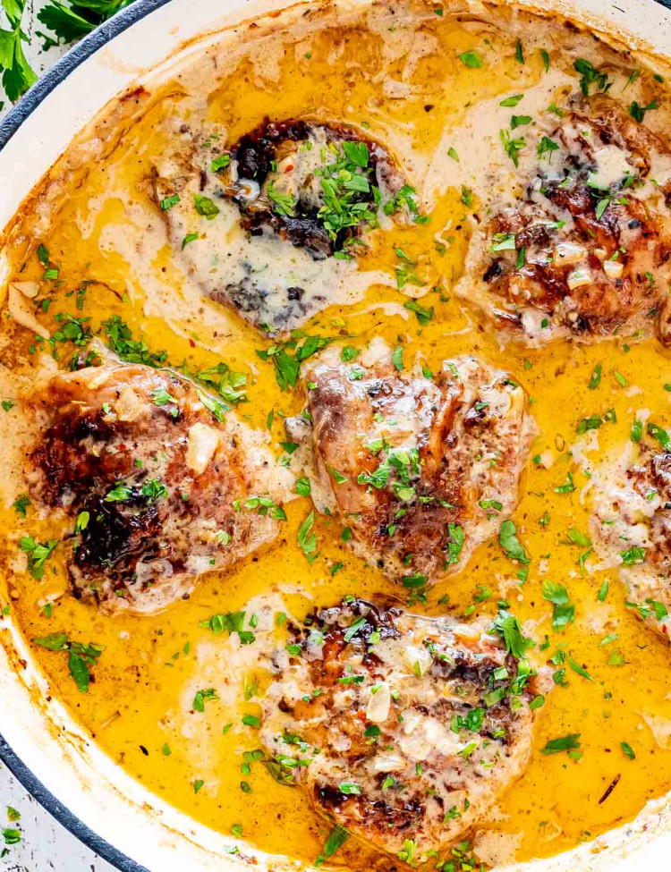 smothered chicken with gravy in a skillet garnished with parsley.