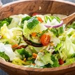 a serving spoon lifting up some salad over a tossed salad bowl.