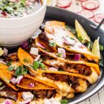 a few birria tacos on a platter with a bowl of birria sauce.