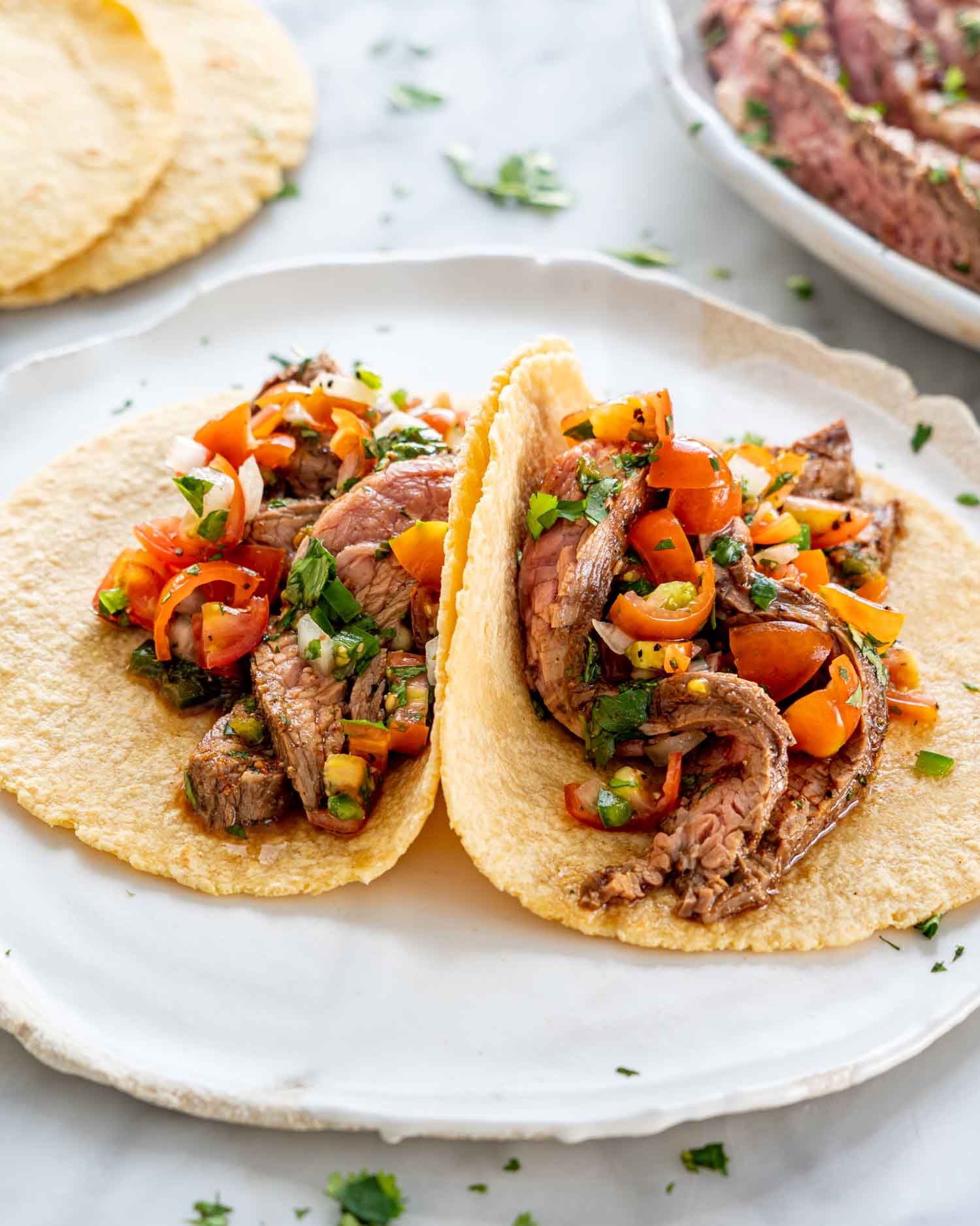two tacos with carne asada on a plate.
