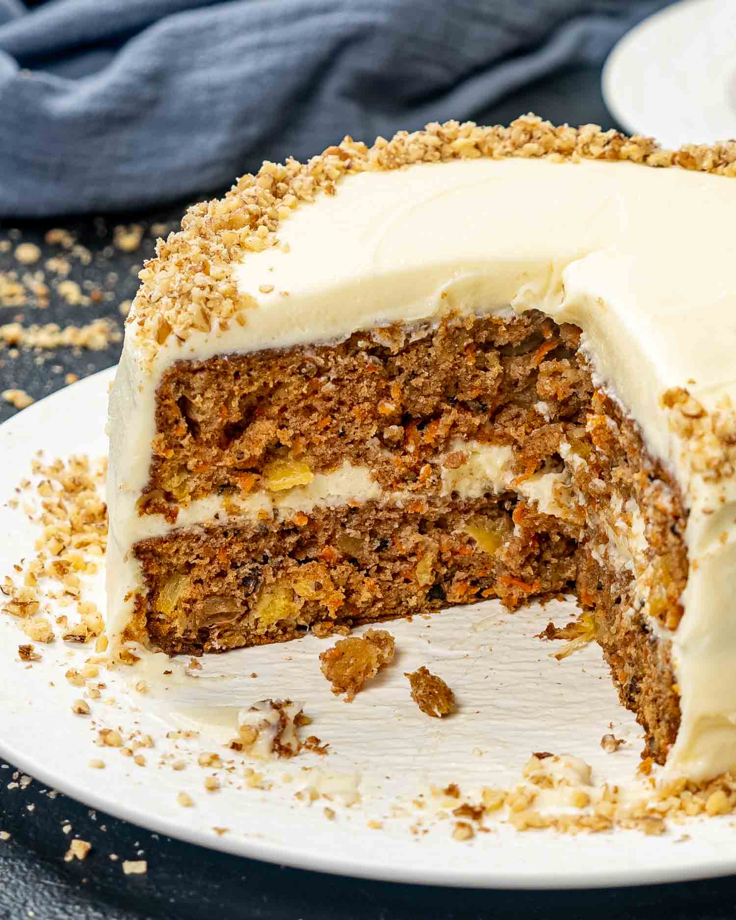a carrot cake on a white cake platter with a few slices missing.