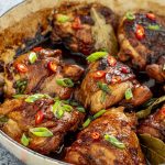 chicken adobo in a braiser garnished with green onions and red chilies.