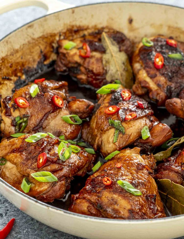 chicken adobo in a braiser garnished with green onions and red chilies.