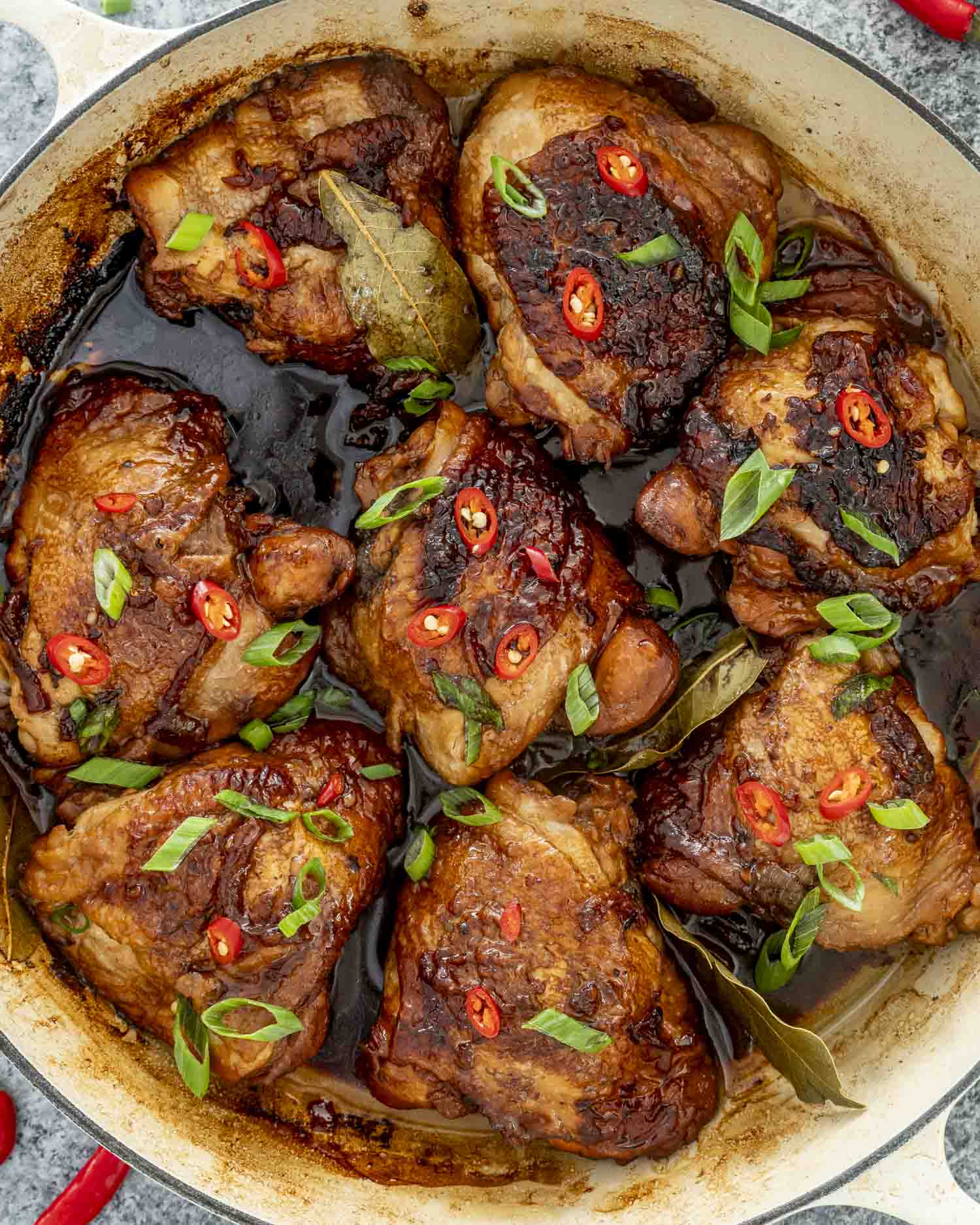 chicken adobo in a braiser garnished with green onions and red chilies.