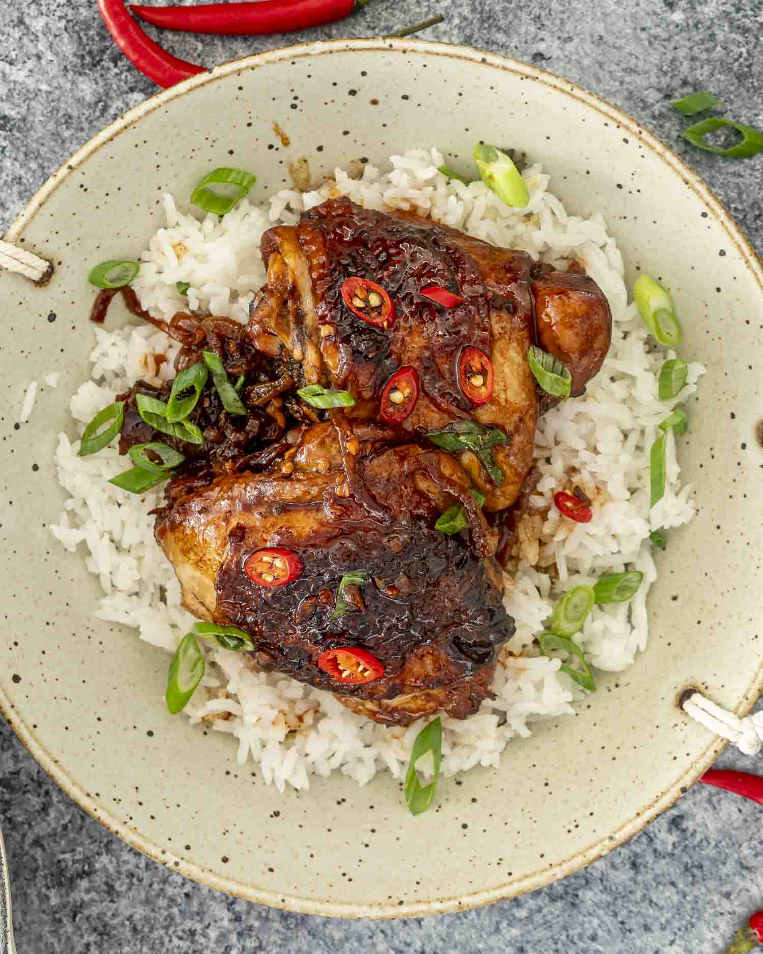 two chicken adobo thighs over a bed of rice garnished with green onions.