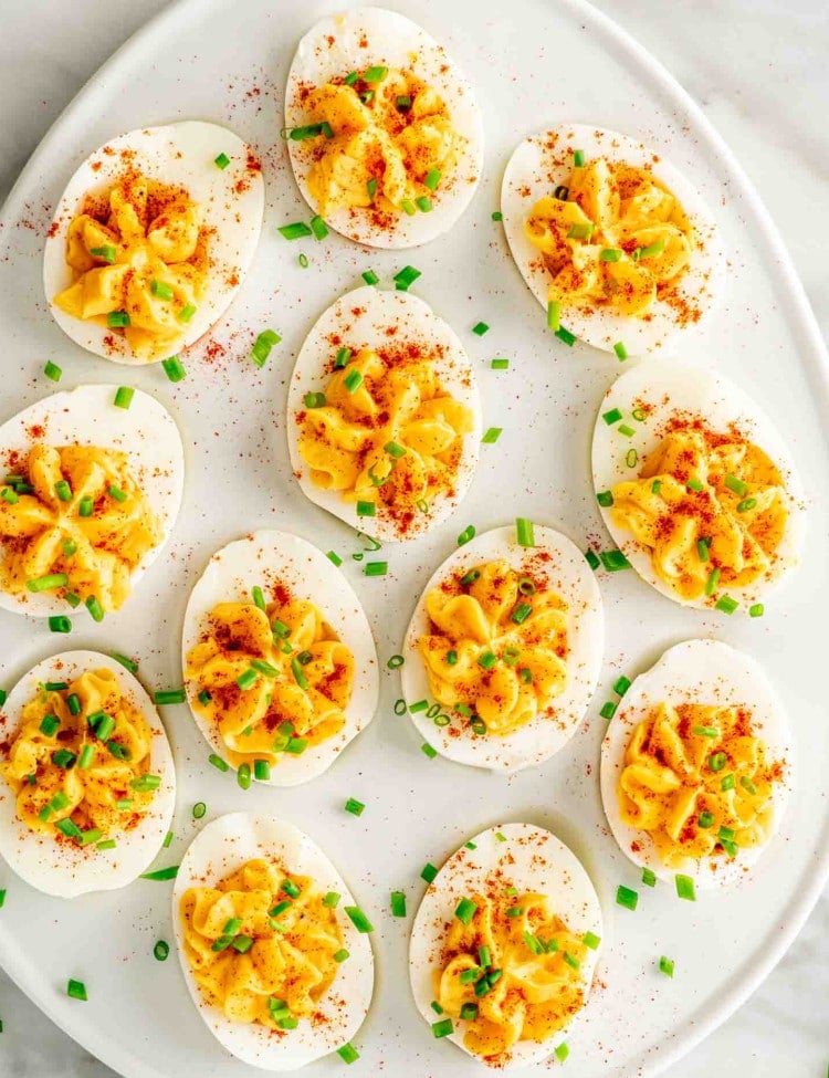 deviled eggs on a serving platter garnished with paprika and chives.