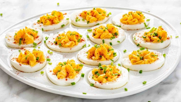 deviled eggs on a serving platter garnished with paprika and chives.