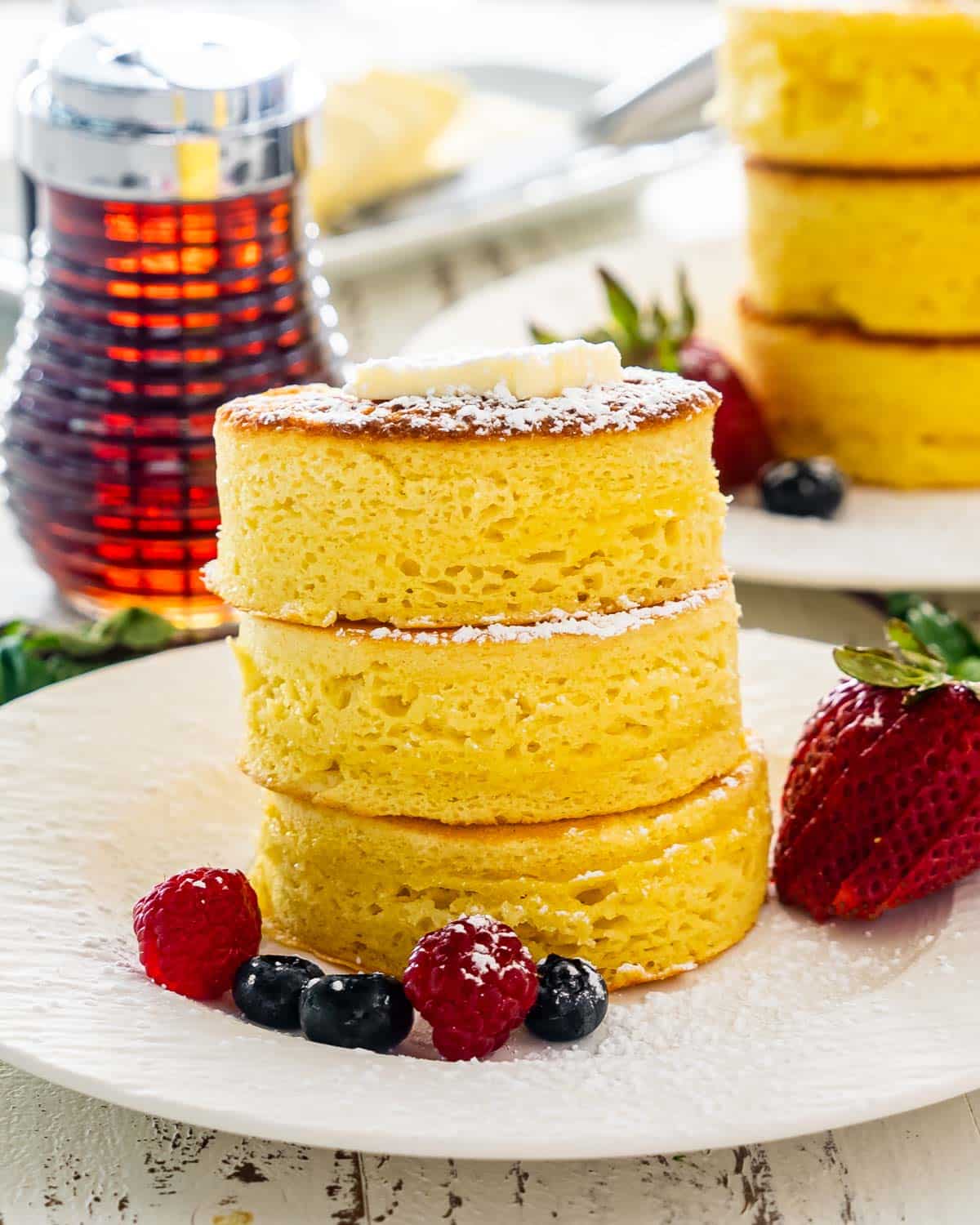 a stack of 3 japanese pancakes on a white plate with some berries around it.