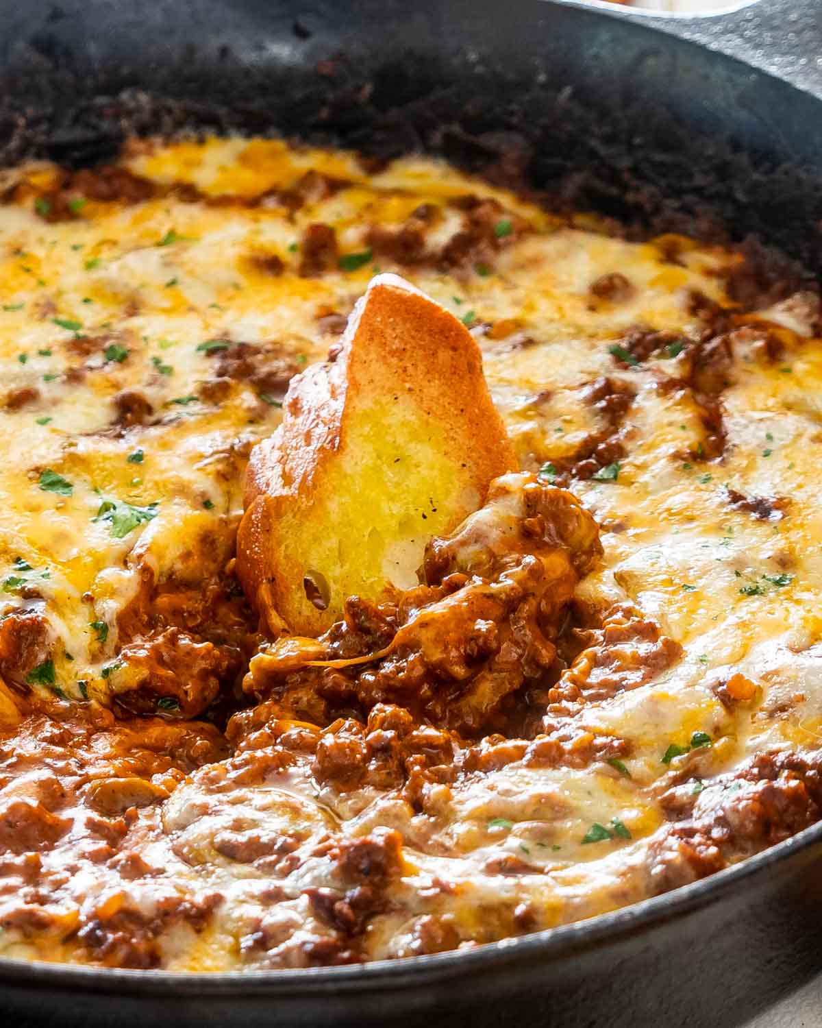 sloppy joe dip in a black skillet with a piece of toasted bread in it.