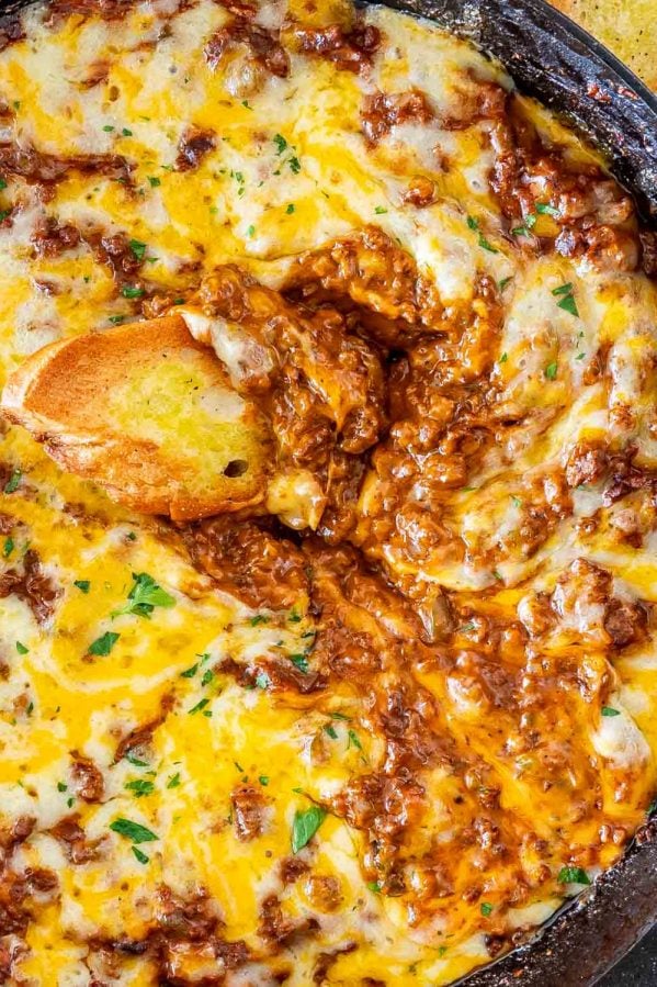 sloppy joe dip in a black skillet with a piece of toasted bread in it.