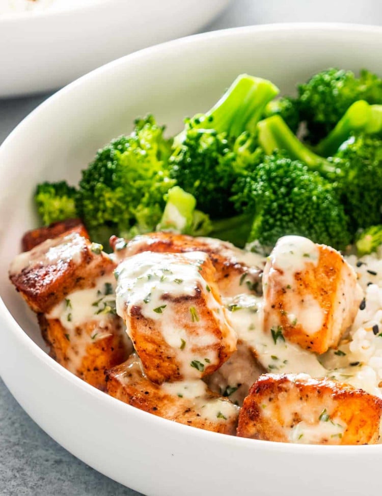 air fryer salmon with creamy garlic sauce in a white bowl with rice and broccoli.