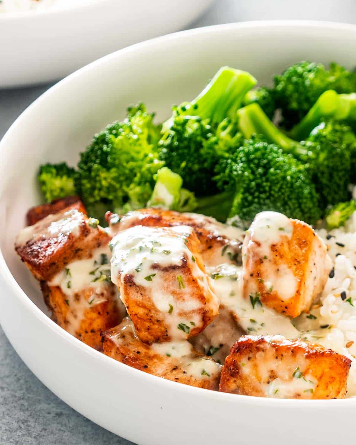air fryer salmon with creamy garlic sauce in a white bowl with rice and broccoli.
