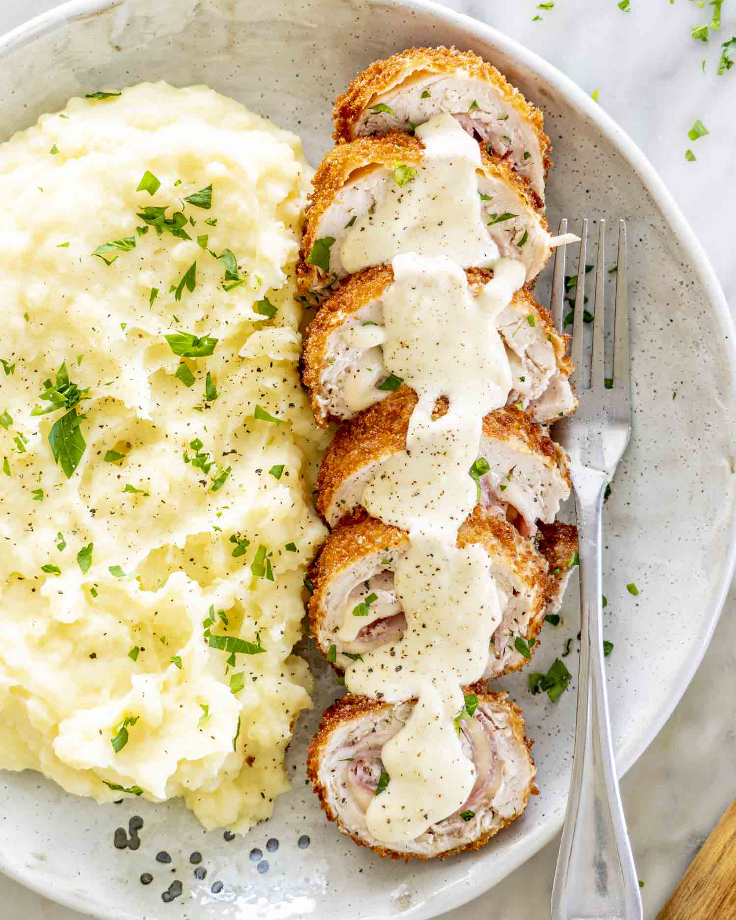 sliced up chicken cordon-bleu with sauce on a plate with mashed potatoes.