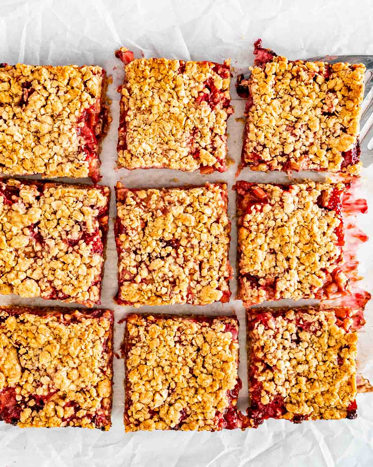 strawberry rhubarb bars cut into pieces on a piece of parchment paper.
