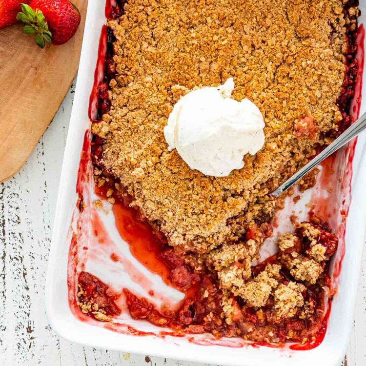 strawberry rhubarb crisp in a baking dish with a scoop of vanilla ice cream in the middle.