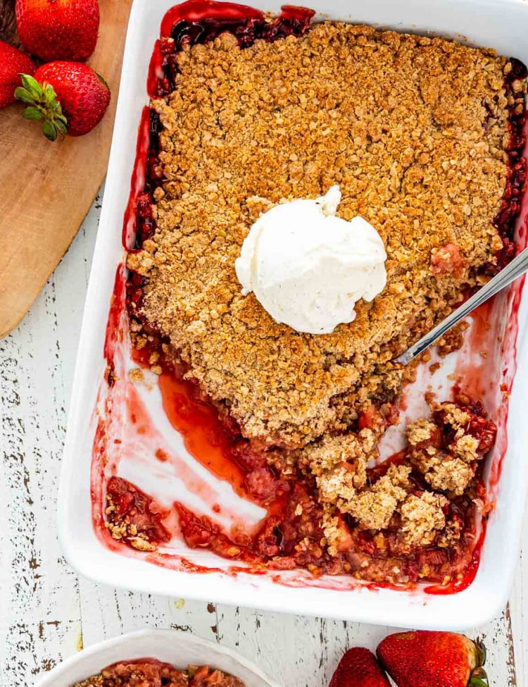 strawberry rhubarb crisp in a baking dish with a scoop of vanilla ice cream in the middle.