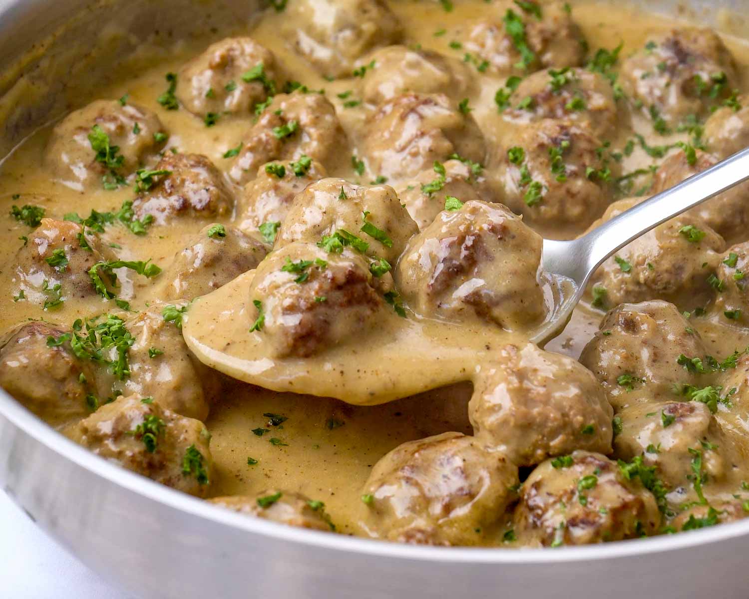 An overhead view of a white bowl containing eight beef Swedish meatballs in creamy gravy on top of a bed of egg noodles