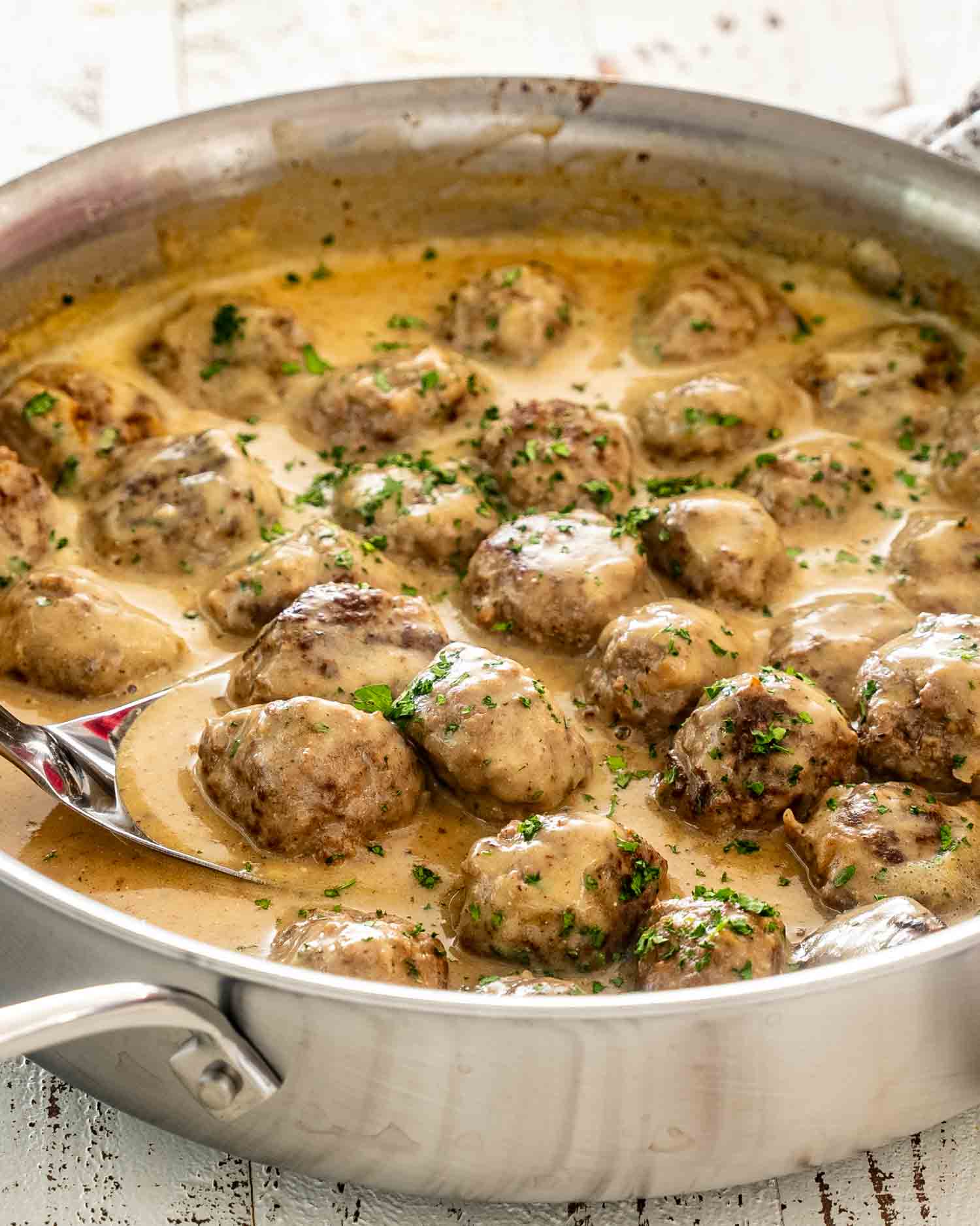 A close up angled shot of several beef Swedish meatballs with gravy and chopped parsley resting on a bed of egg noodles.