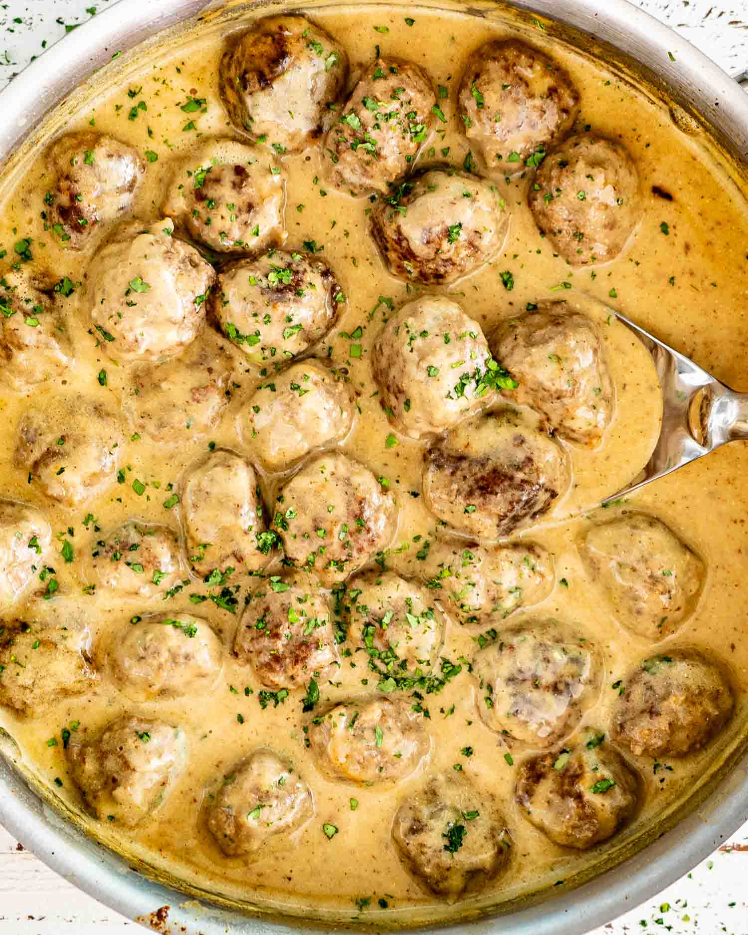A top down view of a stainless steel skillet filled with twenty four beef Swedish meatballs simmering in a creamy brown gravy.