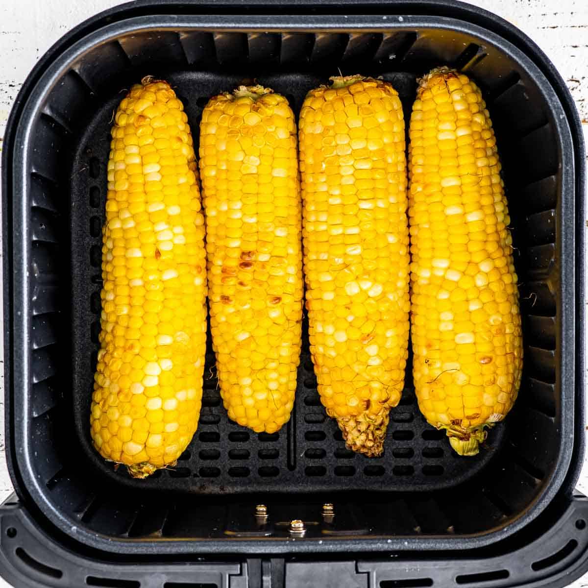 cooked corn on the cob in an air fryer basket.