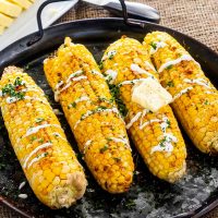 corn on the cob with sour cream, paprika on a platter.