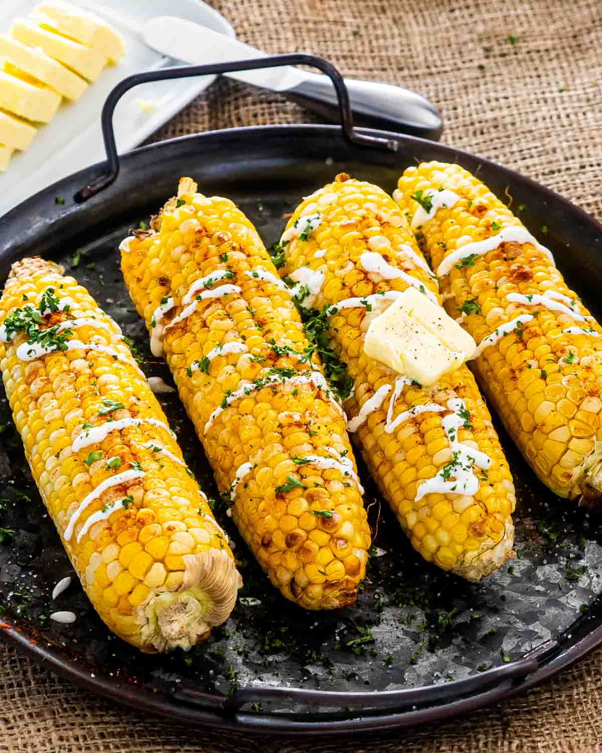 corn on the cob with sour cream, paprika on a platter.