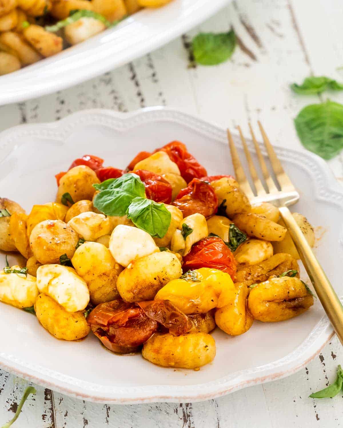 a serving of caprese gnocchi in a white plate with a gold fork.