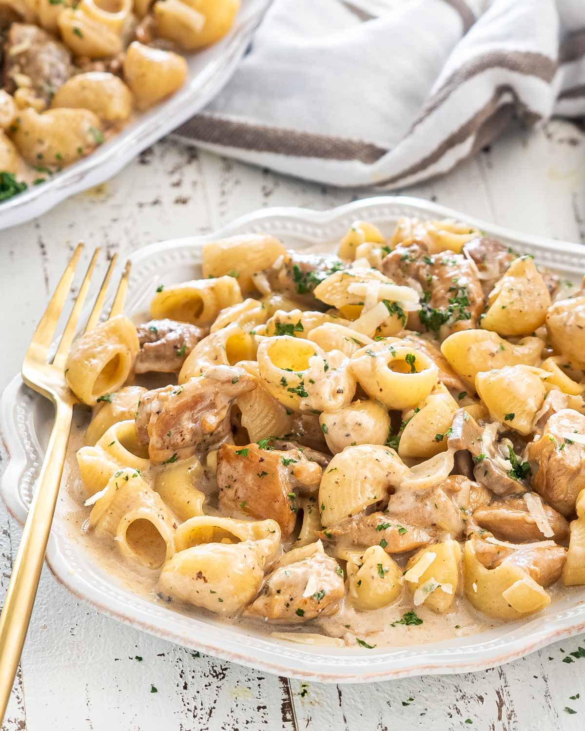 a serving of creamy chicken marsala pasta in a white plate with a gold fork.