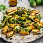 sweet and sour air fryer brussels sprouts in a white platter with a serving spoon.