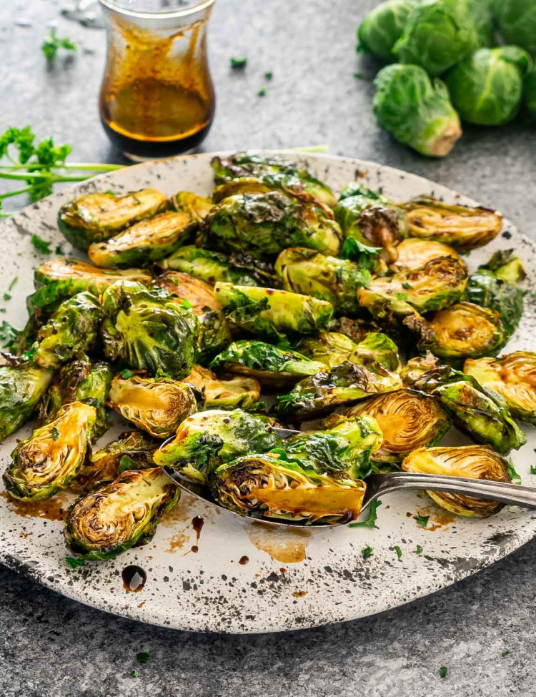 sweet and sour air fryer brussels sprouts in a white platter with a serving spoon.