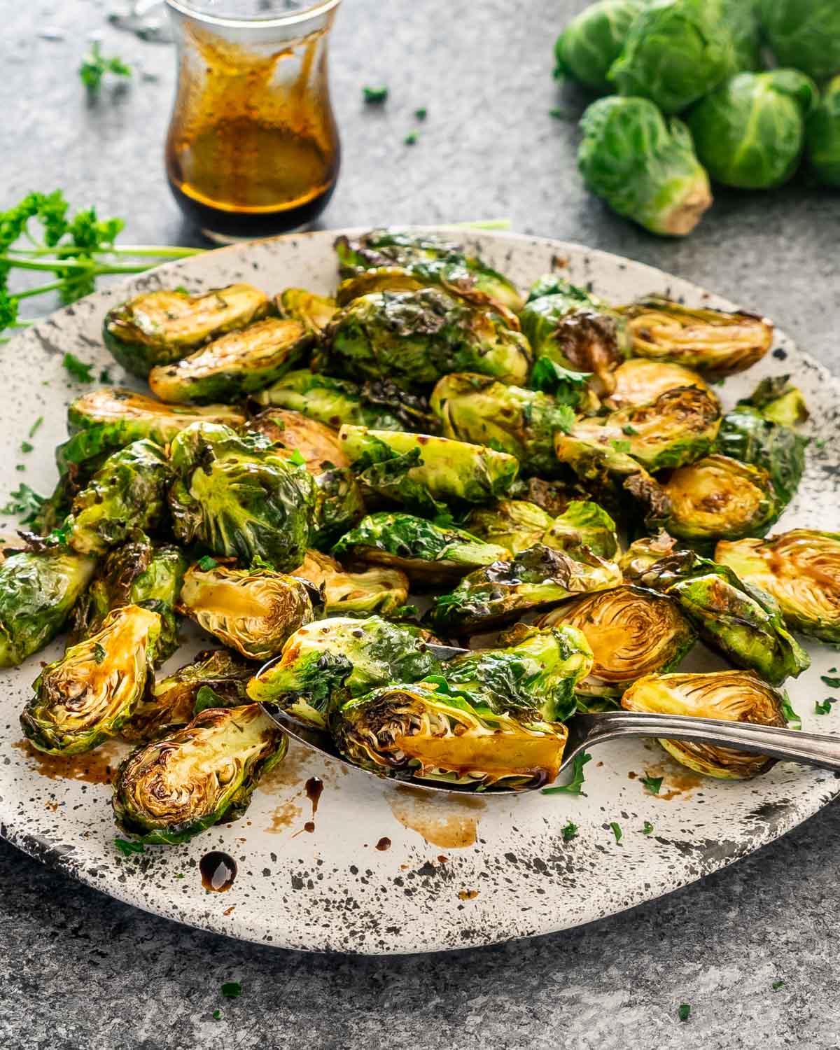 sweet and sour air fryer brussels sprouts in a white platter with a serving spoon.