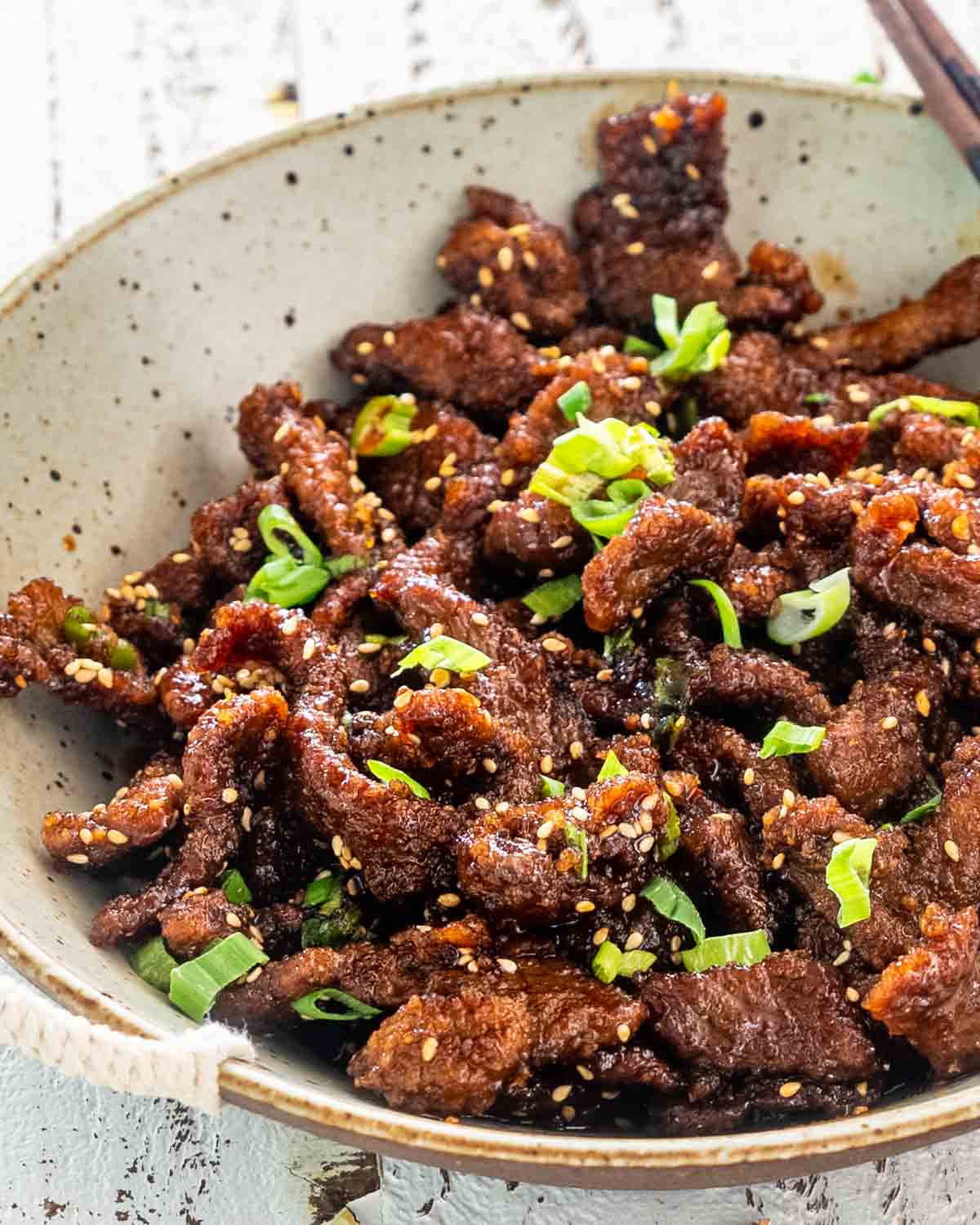 crispy sticky beef in a plate garnished with green onions.