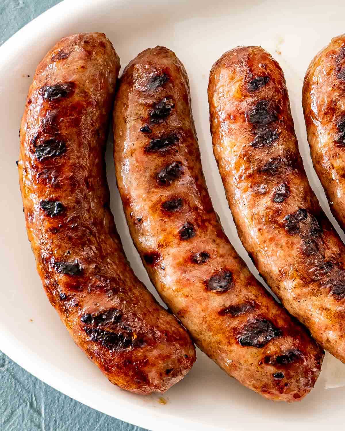 grilled bratwursts on a white plate.