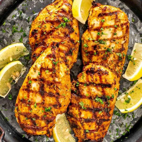 grilled chicken breast on a metal platter garnished with lemon wedges and parsley.