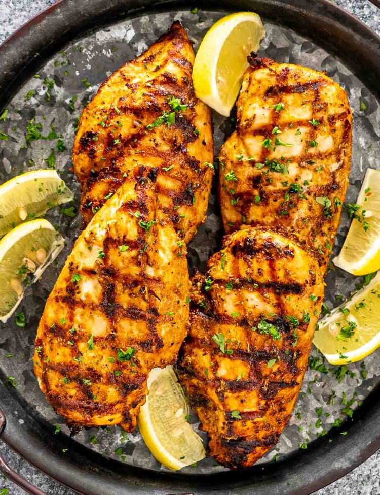 grilled chicken breast on a metal platter garnished with lemon wedges and parsley.