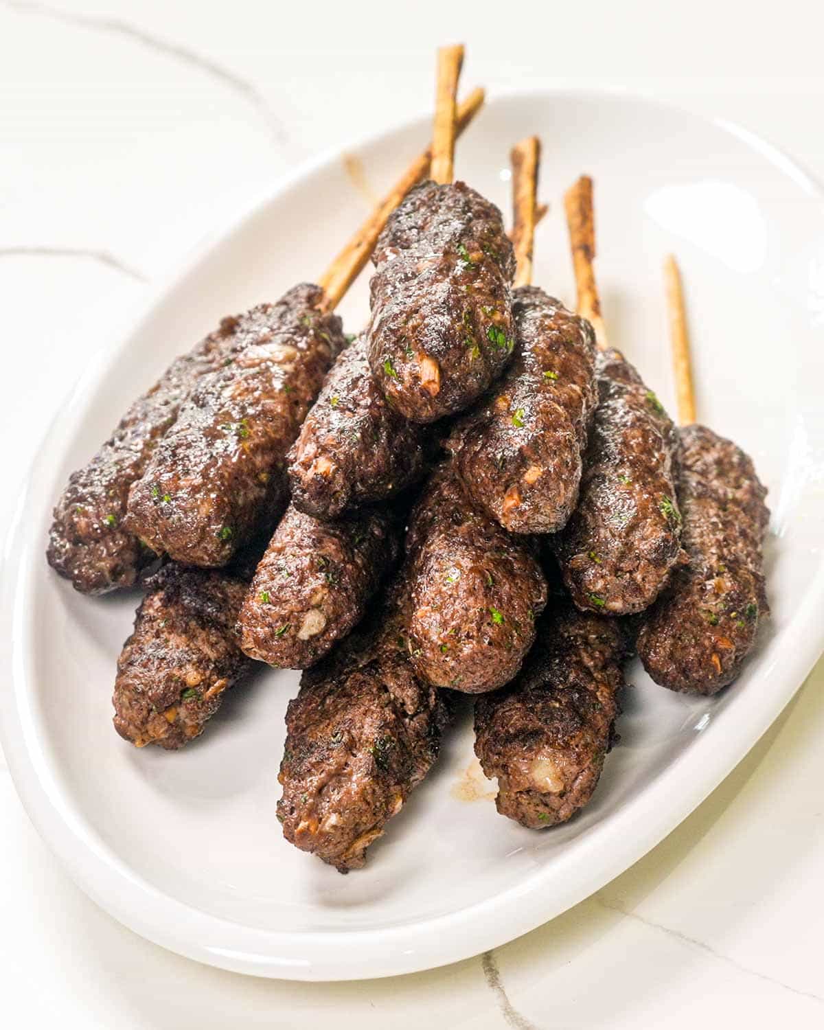 a few freshly cooked beef koftas on a white platter.