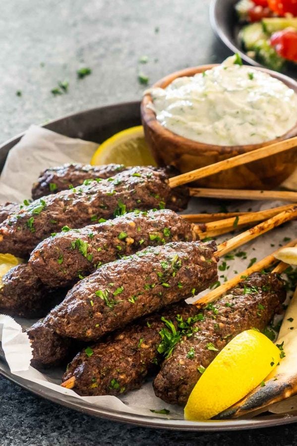 a few beef koftas on a plate with some pitas garnished with parsley next to tzatziki sauce.
