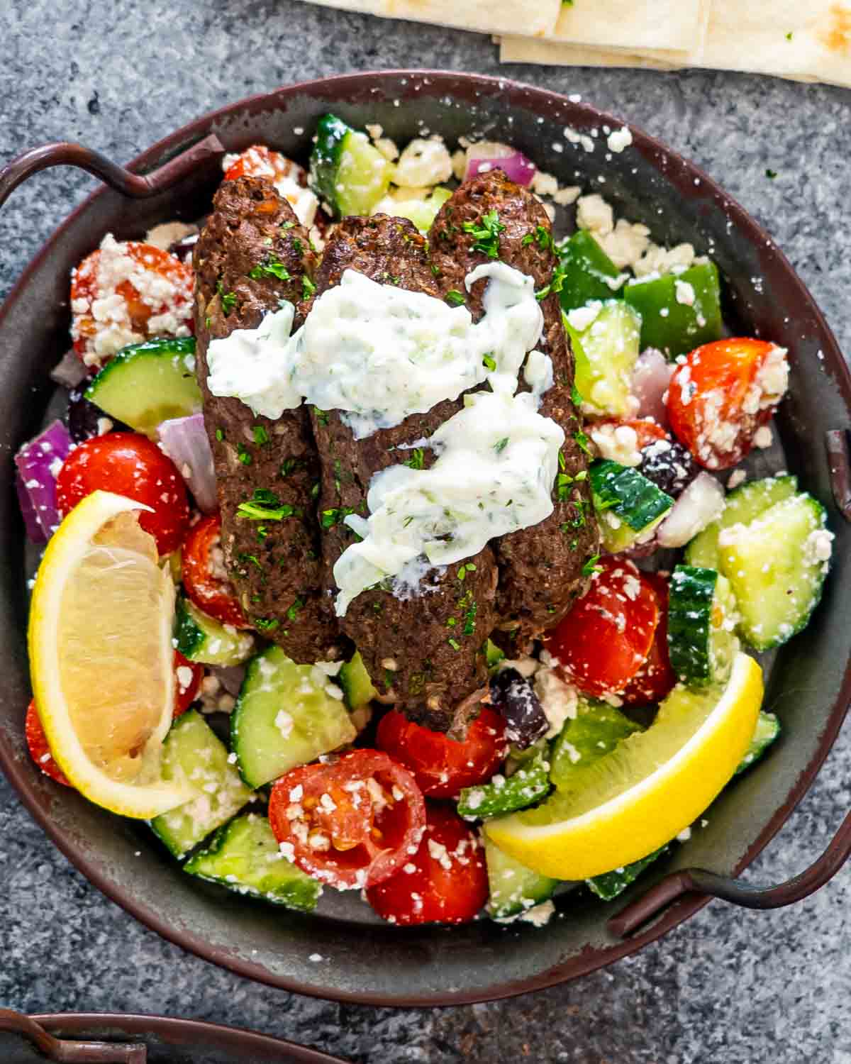 3 beef koftas topped with tzatziki on top of a greek salad.