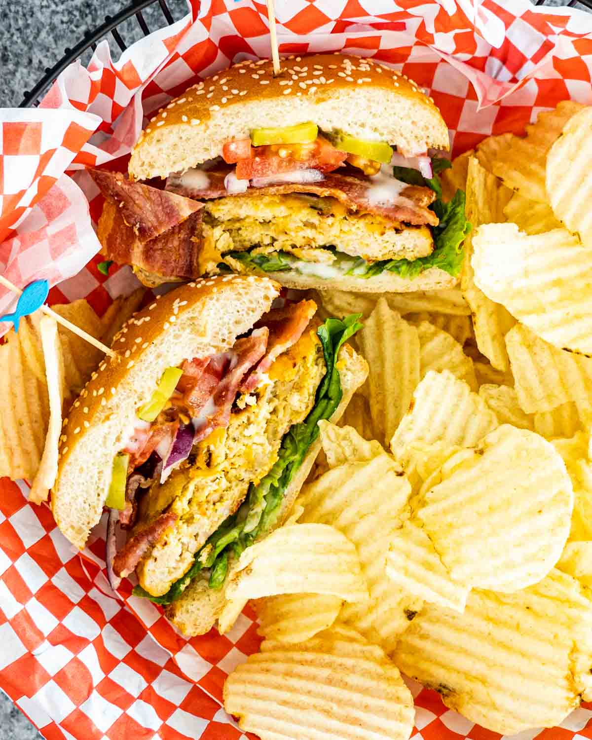 a chicken ranch burger cut in half in a serving platter with potato chips.