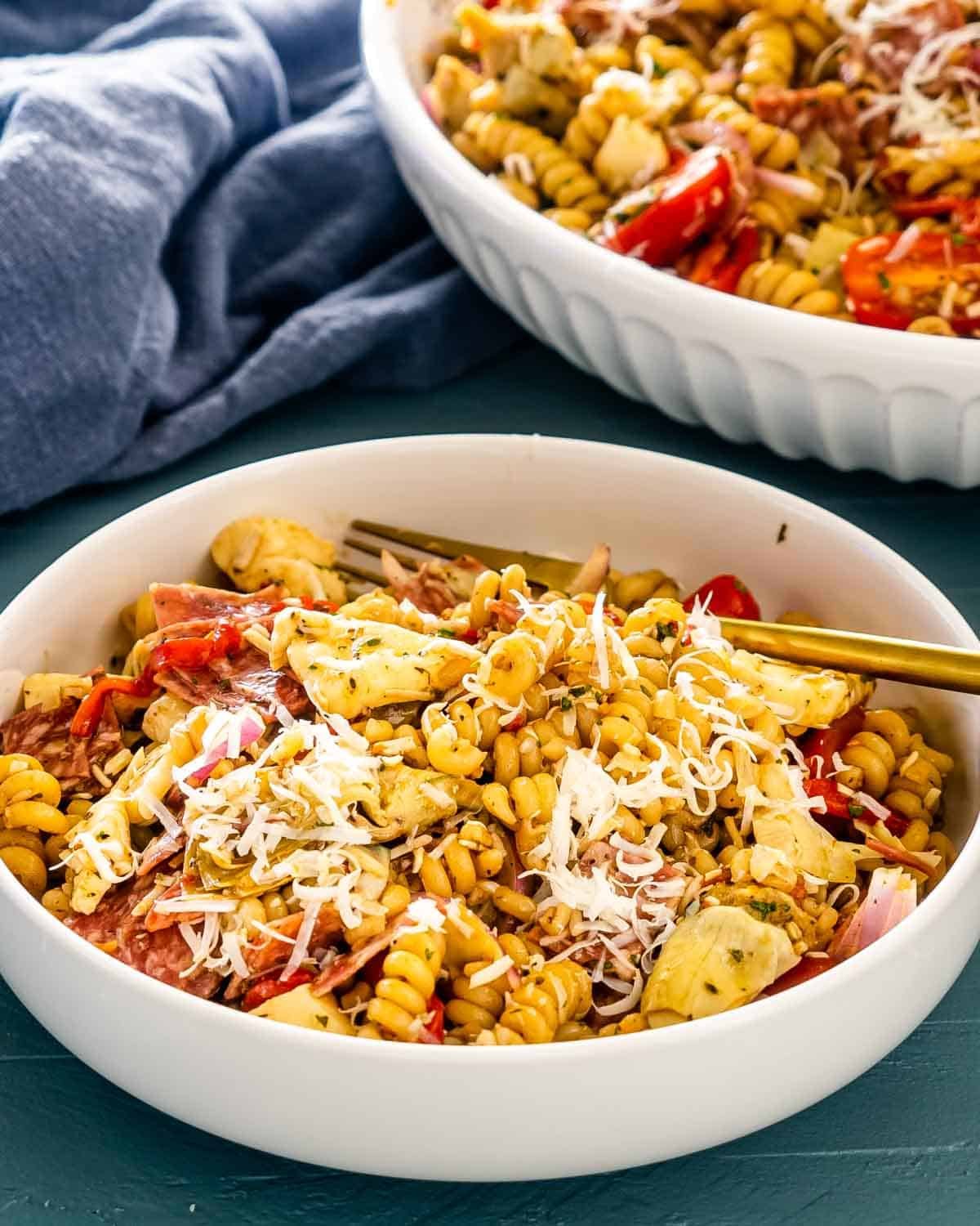 a serving of antipasto pasta salad in a white bowl with a golden fork.