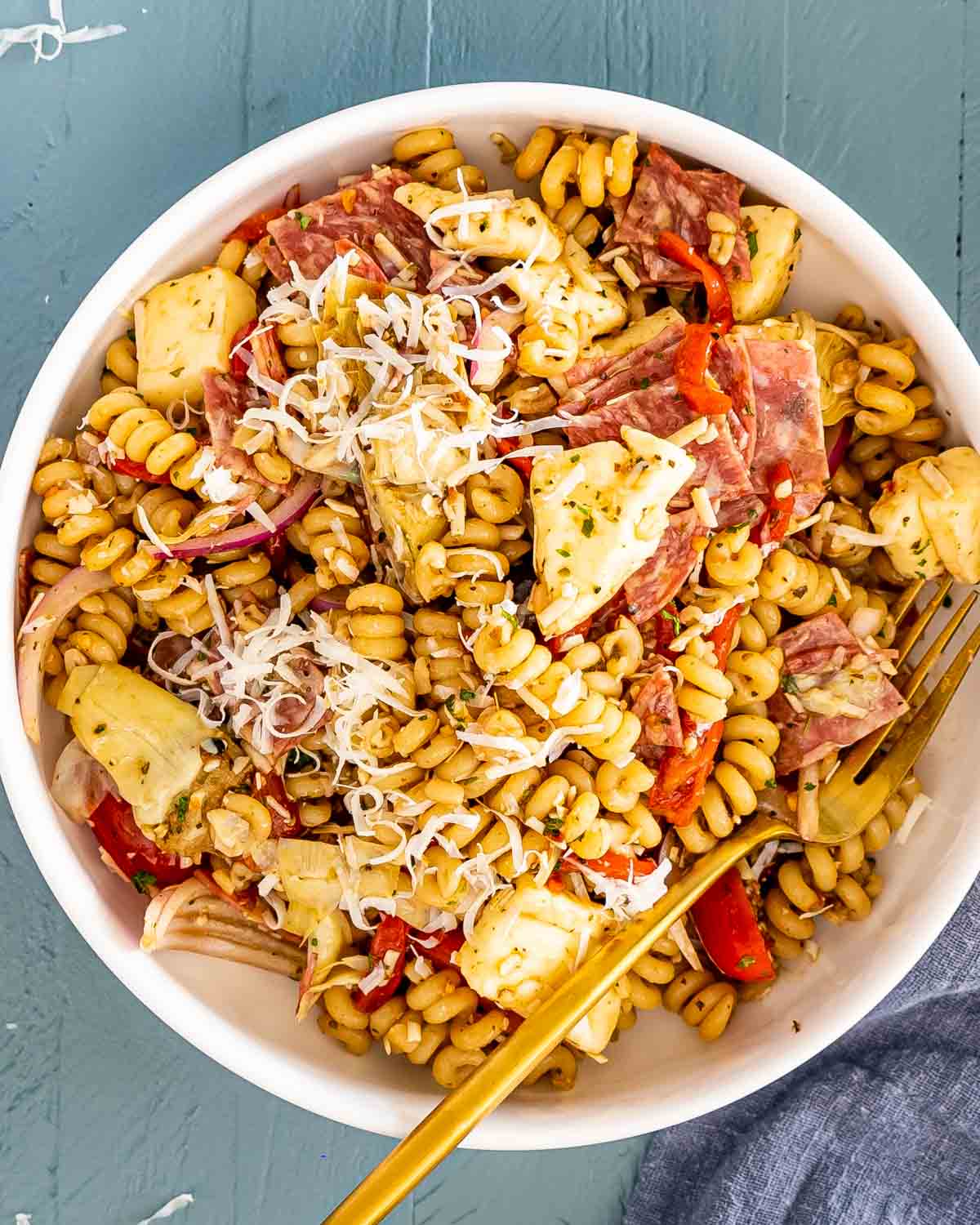 a serving of antipasto pasta salad in a white bowl with a golden fork.