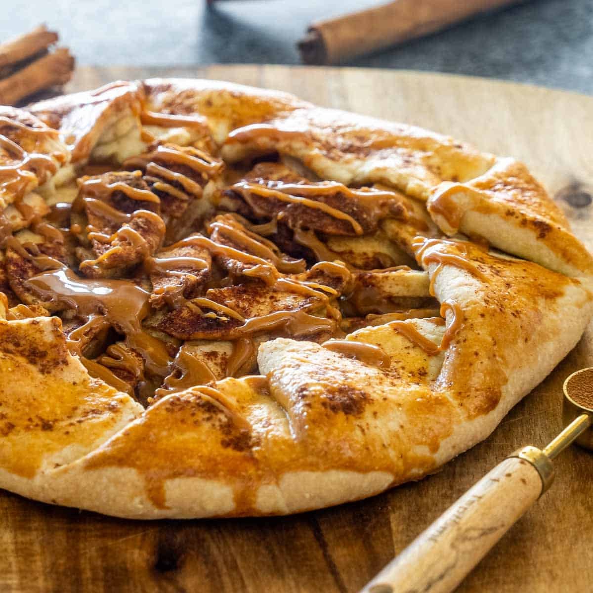 a freshly made apple galette with caramel on a cutting board.
