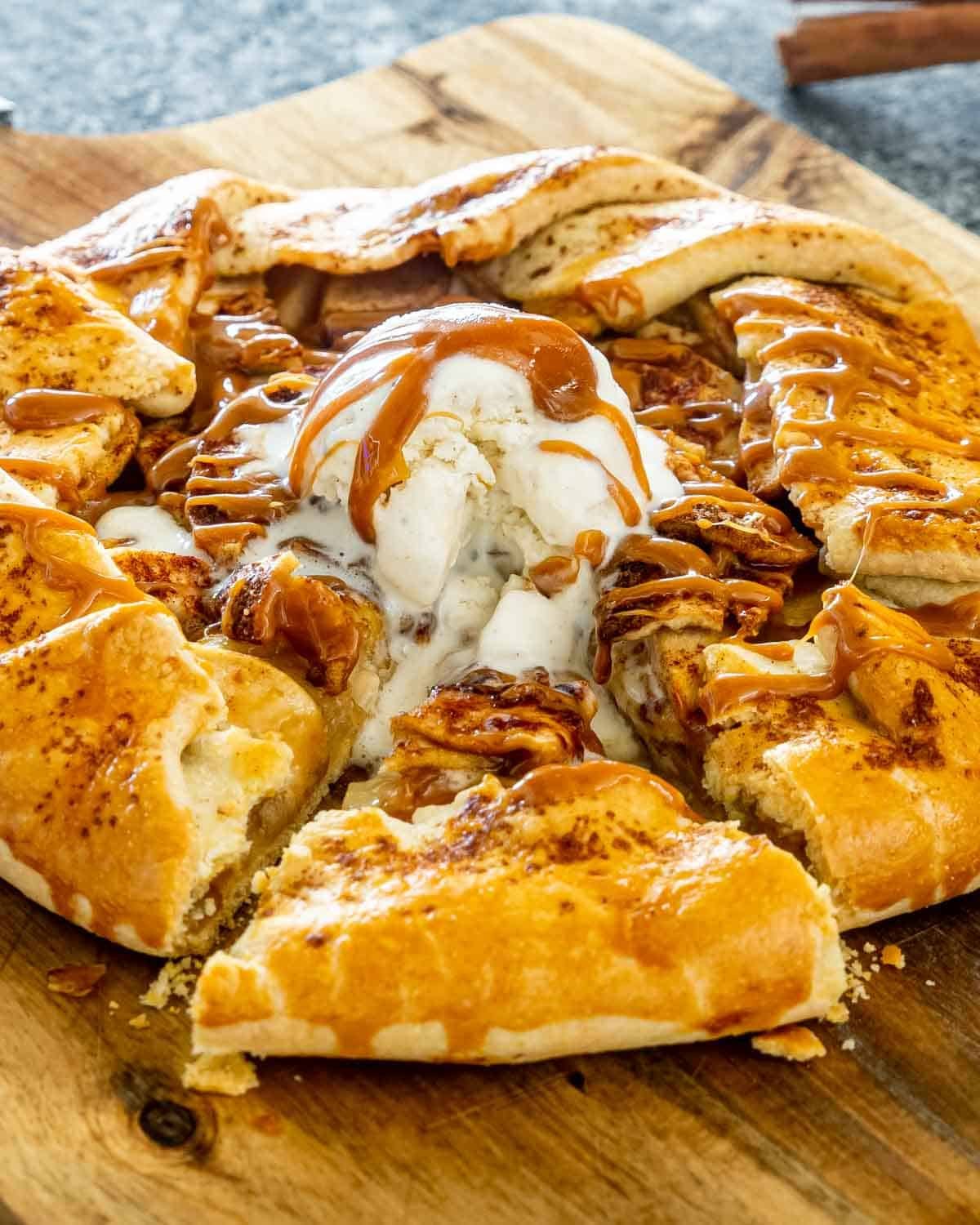 an apple galette with a scoop of ice cream and caramel topping with a slice cut out.